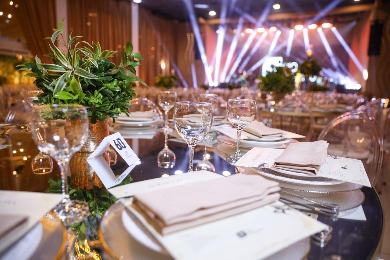 Detalhe de mesa do Celebration — cristal, vegetação e menu CIO