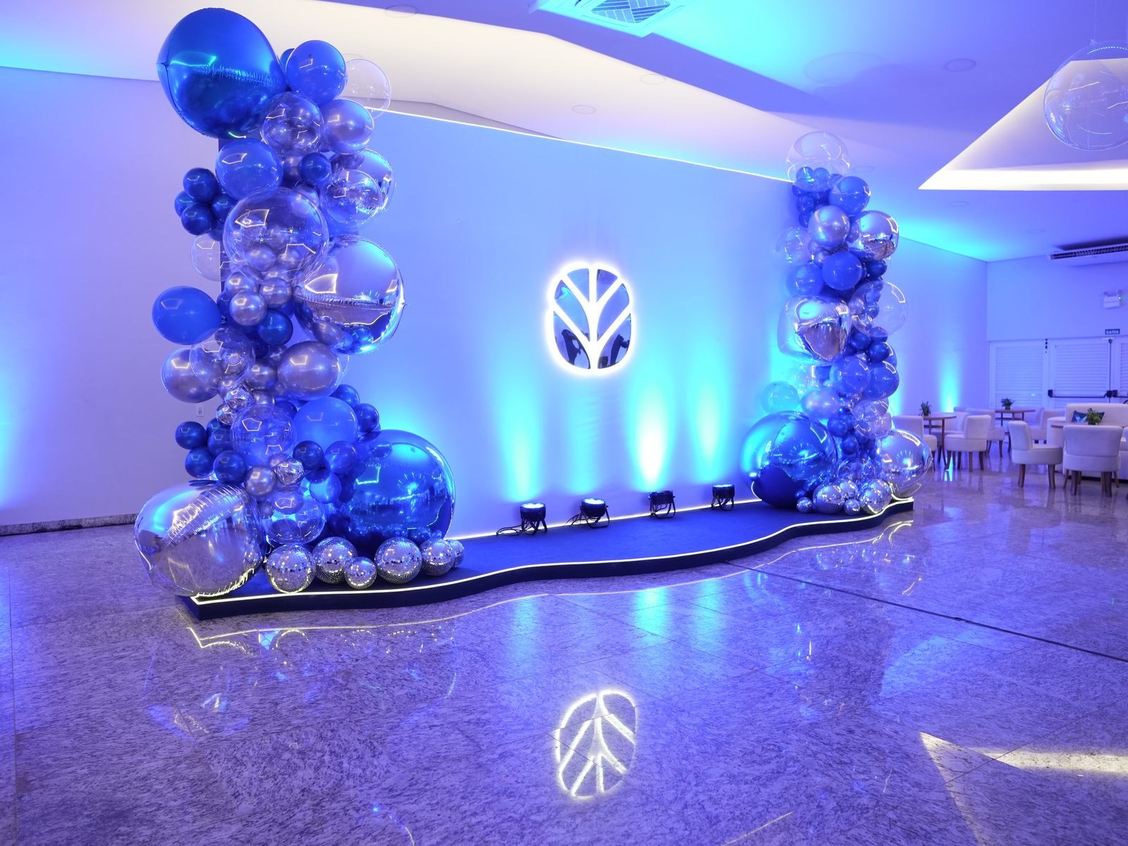 Backdrop com logo New Holland iluminado e decoração de balões azul e prata